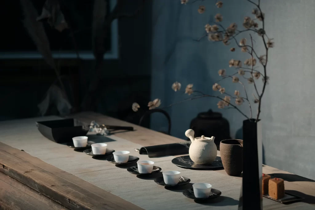A quiet invitation to tea: two white teacups and a charming teapot rest on an aged wooden table bathed in soft sunlight.