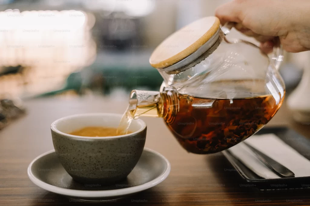 It’s a photograph of a cup of tea. The tea is a dark amber color and sits in a clear glass mug. There is a lemon wedge resting on the rim of the mug. The mug is sitting on a wooden table.