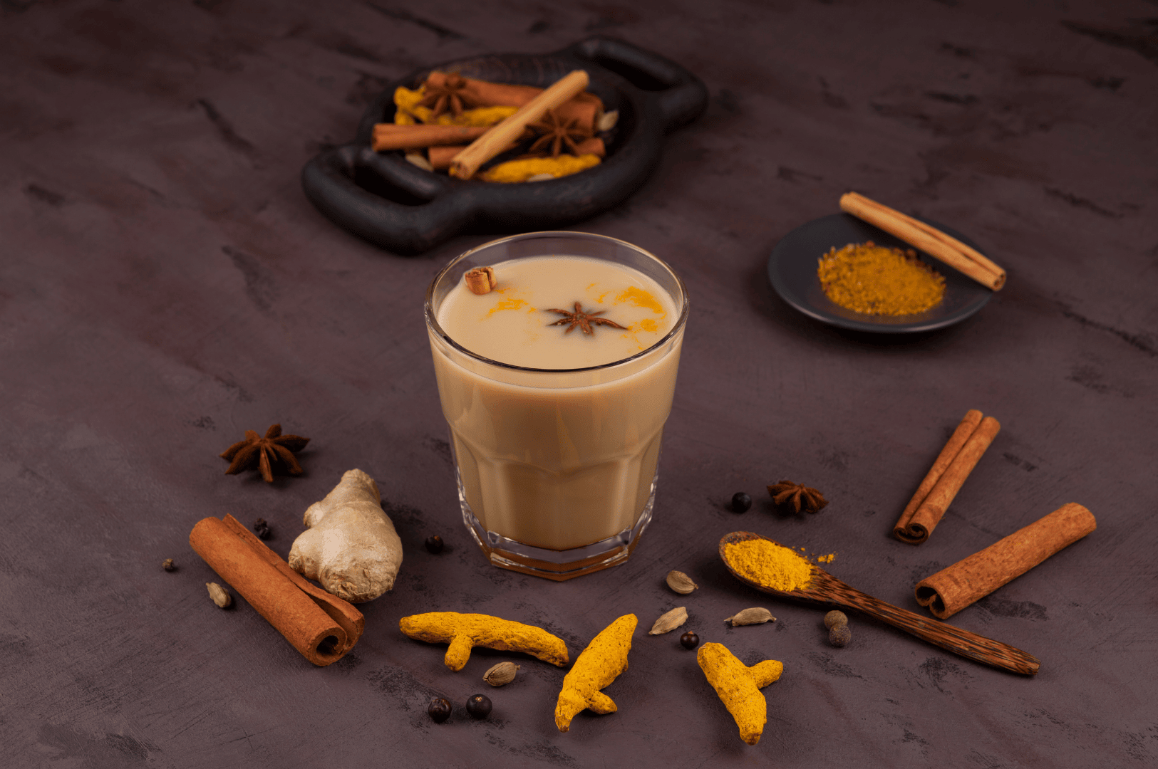 Glass of golden masala chai inspired chai tea surrounded by whole spices including fresh ginger, ground ginger, green cardamom pods, star anise, and cinnamon sticks, evoking authentic masala chai traditions of the Indian subcontinent. This spiced tea blends black tea, darjeeling tea, assam tea, or green tea with chai masala powder, tea masala, and aromatic spices from tea plantations in South India. Perfect for tea drinkers and indian tea drinking culture, masala chai translates to traditional Indian tea brewed with milk and sugar, oat milk, or steamed milk, sweetened with brown sugar, coconut sugar, or maple syrup. Whether enjoyed as a chai tea latte, chai latte, milky tea, or milky cup, it’s a hot cup of comfort. Made with loose tea, black tea bags, or ctc tea, this cup of masala chai or cup of chai can be aerate chai for froth. Rooted in indian masala chai heritage, it reflects indian tea culture, tea trade, tea board standards, tea production, and tea sellers or tea vendors sourcing all the spices from south asian grocery stores. Served by chai vendors at tea stalls, local coffee shop, or coffee shops, it’s the perfect cup for tea breaks, drinking tea, or review recipe moments. Infused with fragrant spices, aromatic herbs, spice mix, fennel seeds, ceylon cinnamon, and tea plant origins, this masala tea celebrates why this recipe remains beloved among tea produced traditions worldwide, prepared with spice grinder precision and ground spices for a rich, flavorful tea brewed experience.