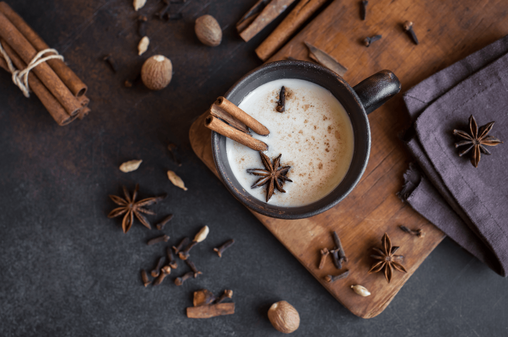 Warm cup of masala chai on a wooden board, garnished with cinnamon sticks and star anise, surrounded by whole spices like green cardamom pods, fennel seeds, ceylon cinnamon, and aromatic herbs. This spiced tea blends black tea, darjeeling tea, assam tea, or green tea with fresh ginger, ground ginger, chai masala powder, tea masala, and fragrant spices from tea plantations in South India. Rooted in indian masala chai traditions, masala chai translates to traditional Indian tea brewed with milk and sugar, oat milk, or steamed milk, sweetened with brown sugar, coconut sugar, or maple syrup. Whether enjoyed as a chai tea latte, chai latte, milky tea, or milky cup, it’s a hot cup of comfort for tea drinkers and indian tea drinking culture. Made with loose tea, black tea bags, or ctc tea, this masala tea is tea brewed with aromatic spices, spice mix, and ground spices using a spice grinder. From tea stalls, local coffee shop, and coffee shops to south asian grocery stores, tea vendors, tea sellers, and chai vendors, the tea trade, tea board, and tea production keep tea produced traditions alive. This perfect cup celebrates indian tea culture, make masala chai heritage, and why this recipe endures across the Indian subcontinent, from tea plant origins to drinking tea moments and tea breaks enjoyed worldwide.