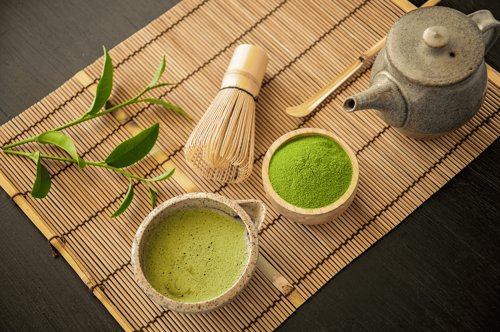 Traditional Japanese tea setup featuring ceremonial grade matcha powder in a wooden bowl with vibrant green color, a ceramic teapot, bamboo whisk, and matcha tea prepared in a ceramic bowl. Surrounded by tea leaves and tools used by tea masters in authentic japanese tea ceremonies, this scene showcases the superior ceremonial matcha produced from first harvest tea plants in Japan. Stone ground to achieve fine particle size and rich umami taste, this highest grade matcha offers strong flavor and smooth texture. Not all matcha is equal—different grades like culinary grade matcha and ceremonial grade vary in quality, taste, and intended use. Culinary grade is often mixed with milk, sugar, or other ingredients for matcha lattes, smoothies, desserts, and baking, while ceremonial matcha is reserved for drinking with hot water. Naoki Matcha and other japanese brands produce high quality matcha determined based on bitterness, sweetness, shade-grown cultivation, and vibrant green color. Matcha grades, including grade matcha powder and culinary grade, are used in cooking, food, and beverages like green tea, sencha, and coffee alternatives. The green tea powder, steamed and ground, reflects the flavor, form, and texture ideal for both traditional and modern uses. This image captures the essence of japanese green tea culture, highlighting the artistry, quality, and ritual behind good matcha.