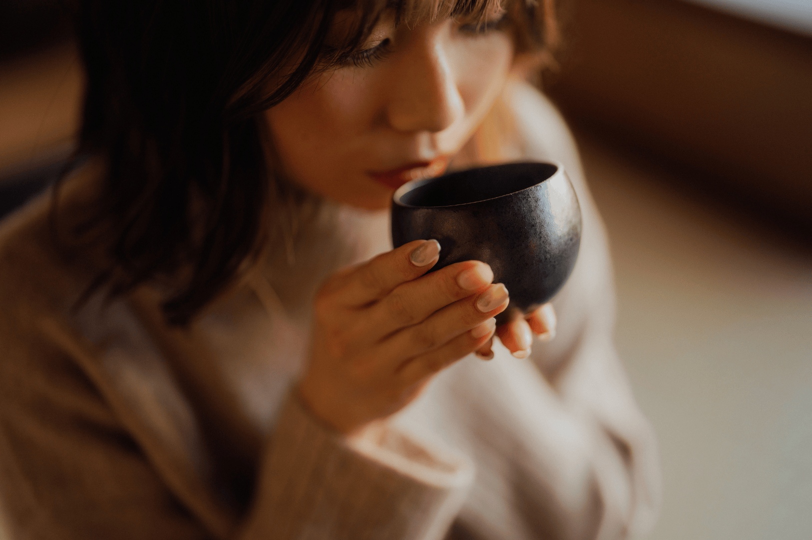 A person gently holds a ceramic cup of vibrant green matcha tea near their mouth, savoring the umami taste and strong flavor of ceremonial grade matcha powder. This intimate moment captures the essence of japanese tea culture, highlighting superior ceremonial matcha from naoki matcha, produced from first harvest tea leaves and shade-grown tea plants in Japan. The smooth texture and vibrant green color of the stone ground matcha powder reflect its highest grade and high quality matcha status. Whether used for matcha lattes, smoothies, desserts, or baking, different grades like culinary grade matcha and ceremonial grade offer distinct taste profiles—from bitter to sweet—determined based on particle size and form. Not all matcha is equal; good matcha reveals a rich umami, ideal for tea ceremonies led by tea masters. Mixed with hot water, milk, sugar, or other ingredients, matcha grades like sencha and culinary grade powder elevate beverages, cooking, and food experiences. This image evokes the artistry of japanese green tea, green tea traditions, and the refined flavor of ceremonial matcha in modern lattes and wellness rituals.