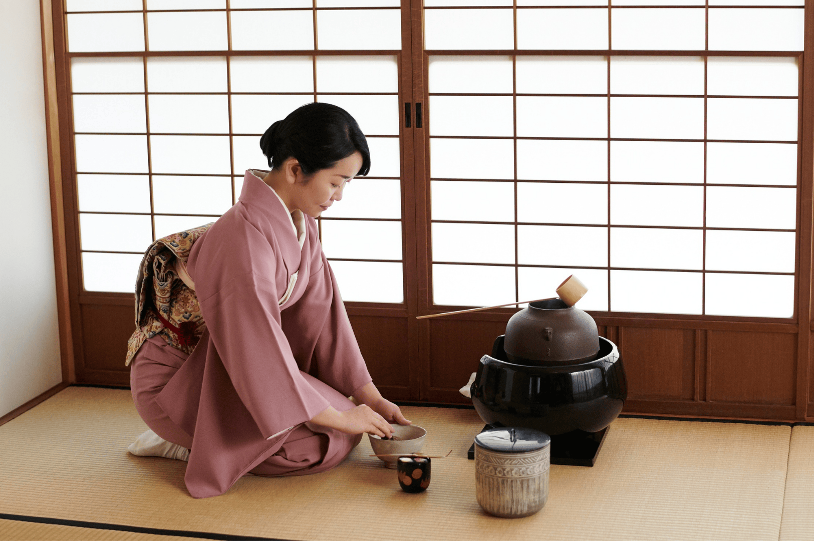 A Japanese tea master kneels on a tatami mat, preparing ceremonial grade matcha using a traditional whisk and tea set during an authentic tea ceremony in Japan. The vibrant green color of the superior ceremonial matcha powder, stone ground from first harvest tea leaves, reflects the highest grade of japanese green tea. This ritual highlights the umami taste, smooth texture, and strong flavor of good matcha, distinguishing it from culinary grade matcha used in matcha lattes, smoothies, desserts, and baking. Naoki Matcha and other premium brands produce high quality matcha determined based on particle size, shade-grown tea plants, and the bitterness or sweetness of the powder. Not all matcha is equal—different grades like culinary grade and ceremonial grade vary in flavor, form, and intended use. While culinary matcha is often mixed with milk, sugar, or other ingredients for beverages and cooking, ceremonial matcha is reserved for drinking with hot water in traditional japanese tea ceremonies. The green tea powder, steamed and ground with precision, offers a rich taste and vibrant color ideal for both food and beverages. Sencha and other japanese teas differ in grade and flavor, but ceremonial matcha remains the pinnacle of matcha grades, produced under sunlight control to enhance umami and reduce bitterness. This image captures the essence of japanese tea culture, showcasing the artistry of tea masters and the refined quality of grade matcha powder.