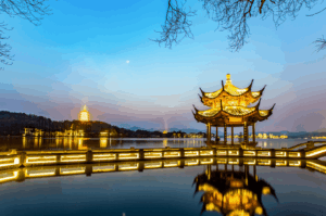 Twilight view of a traditional Chinese pavilion and illuminated pagoda by the tranquil West Lake at Hangzhou, evoking the refined heritage and calming ritual of sipping authentic Longjing tea.