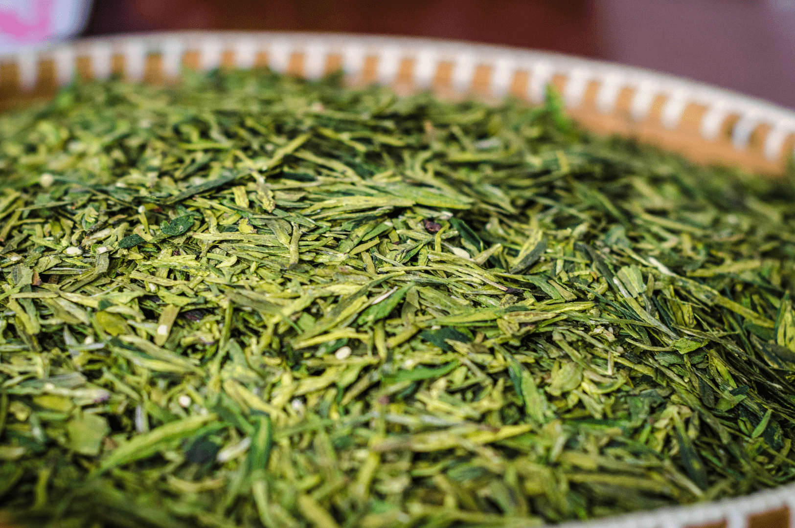 Close-up of premium Chinese Long jing tea leaves on a bamboo tray, showcasing the flat, vibrant green appearance of Dragon Well tea from Hangzhou, prized for its delicate flavor and traditional hand-processing.