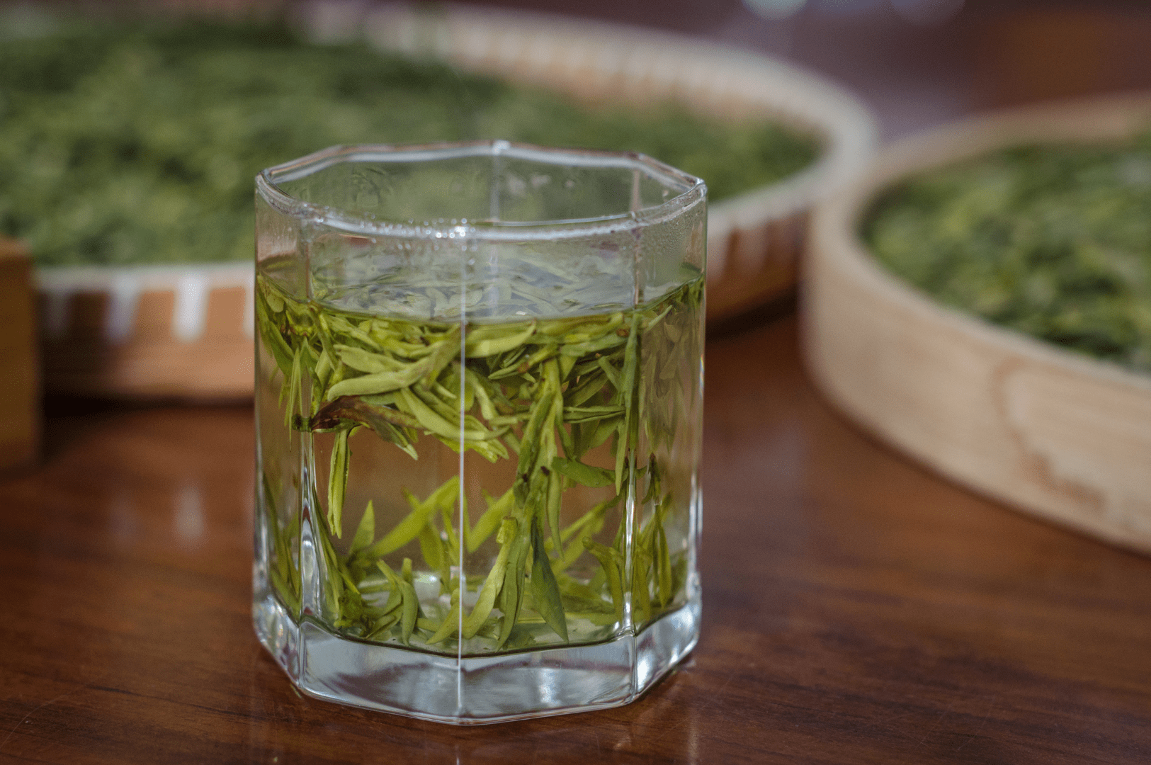 Glass of freshly brewed Long jing tea with vibrant green Dragon Well leaves steeping in hot water, showcasing traditional Chinese tea preparation from Hangzhou’s renowned West Lake region.