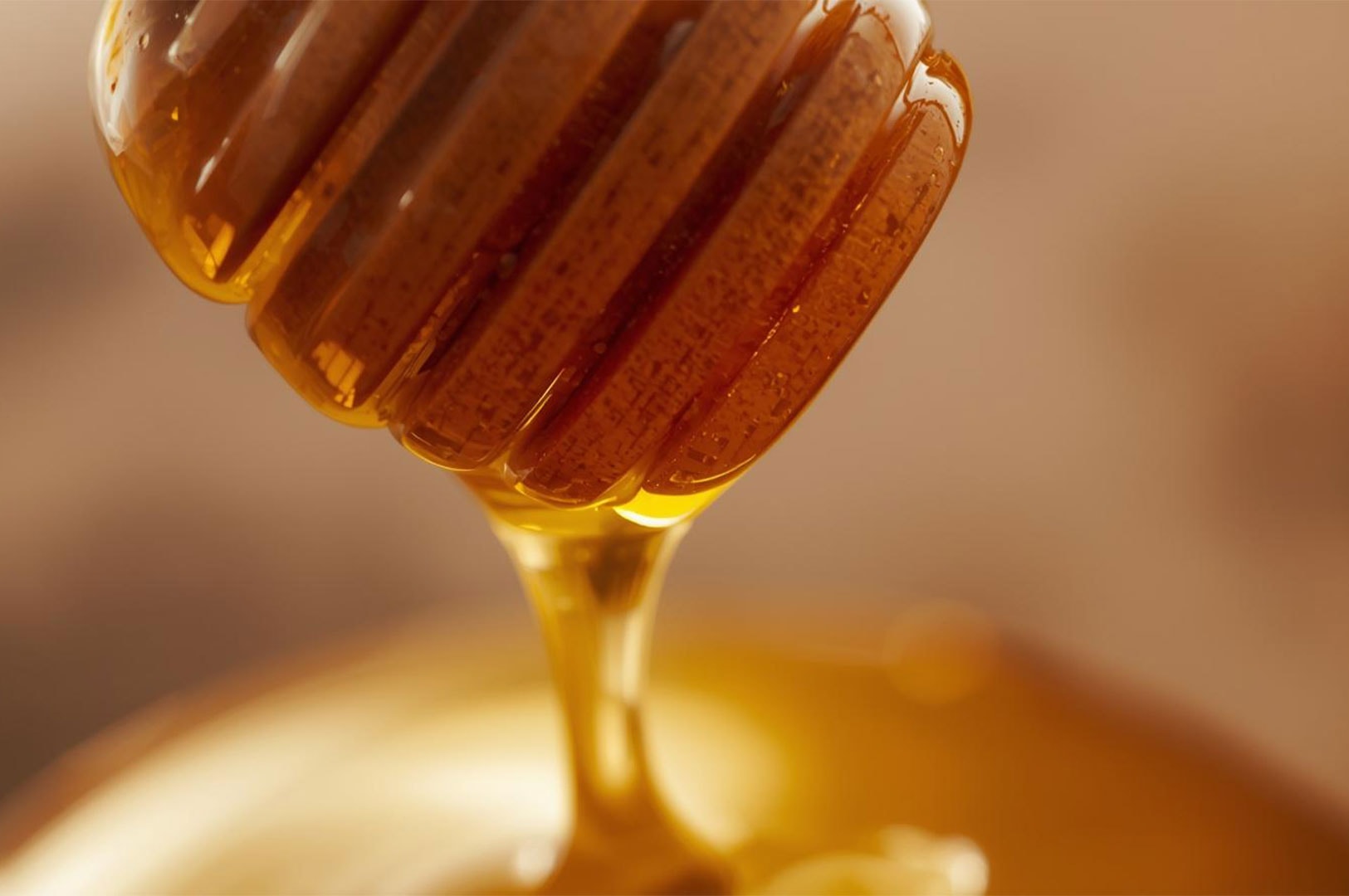 Macro close-up of golden honey dripping slowly from a wooden honey dipper.