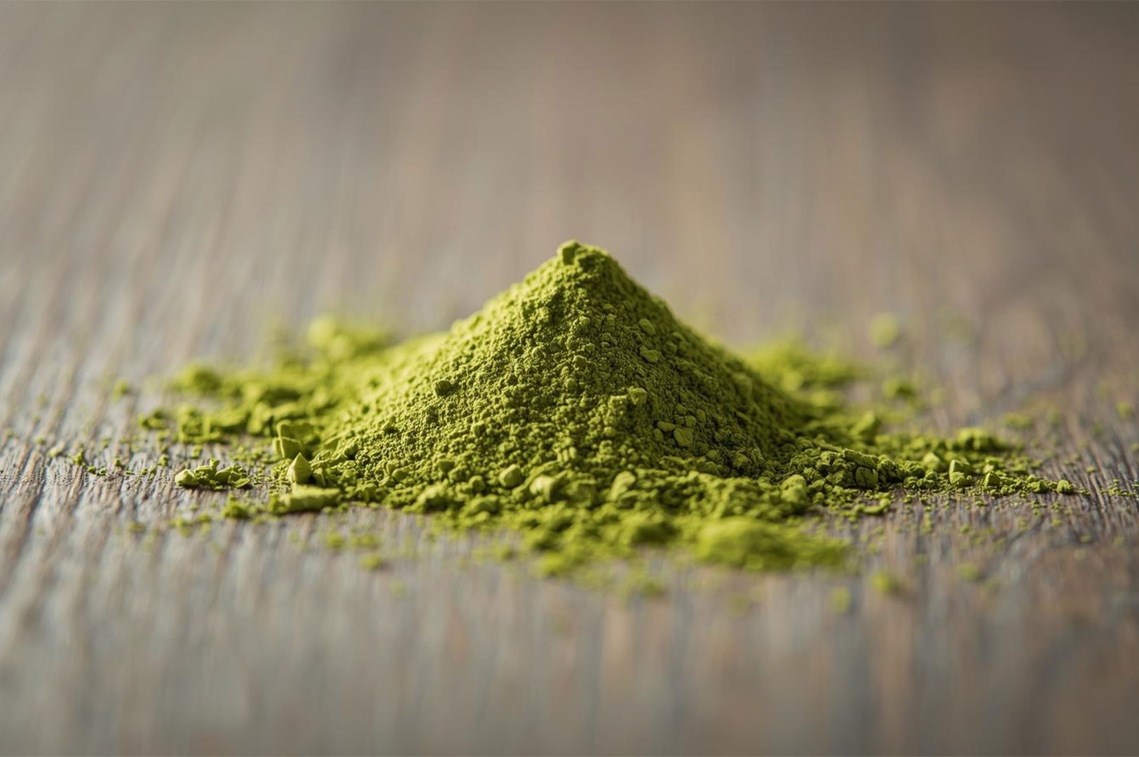 Close-up, low-angle shot of a neat pile of bright green matcha tea powder on a rustic wooden table.
