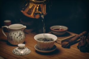 Hot water streams from a golden kettle into a ceramic Gaiwan filled with loose-leaf tea, creating a focused and serene moment of preparation.