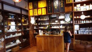 The image depicts a traditional tea shop interior in Singapore's Chinatown, featuring wooden shelves filled with a variety of loose leaf teas, inviting tea lovers to explore the natural goodness and refreshing flavours of green teas and oolong. The tranquil atmosphere offers a perfect moment for indulging in a cup of crafted tea, making it a delightful place to immerse oneself in the world of tea.