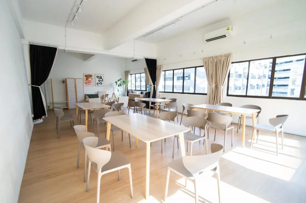 Patrons sit at small tables inside a bustling teahouse featuring shelves lined with canisters and tea cakes. Red lanterns hang from the ceiling, adding a traditional touch to the cozy, narrow interior.
