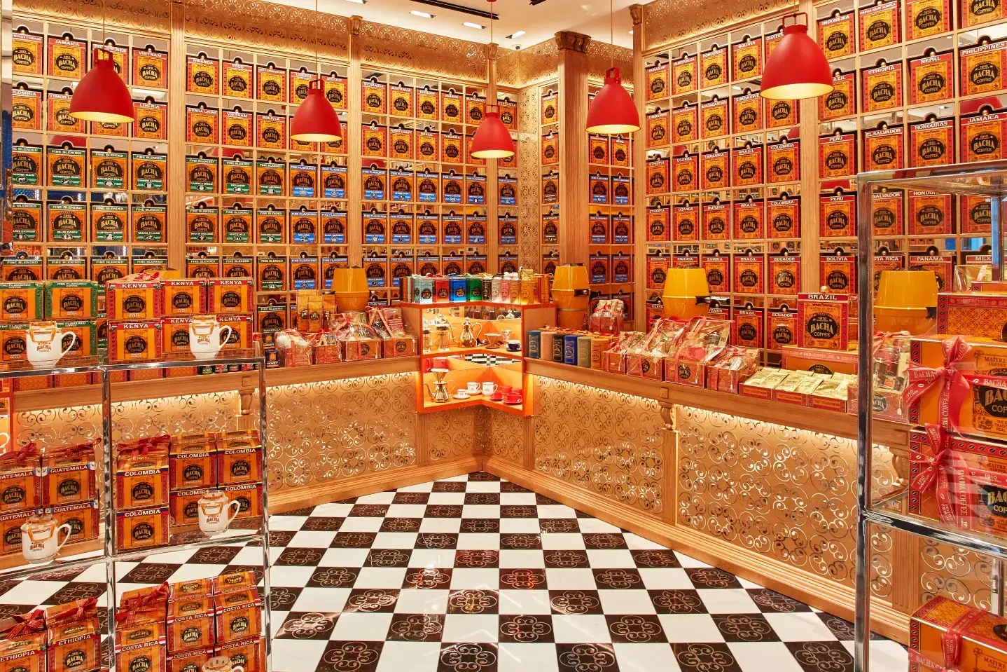 A sprawling wall of ornate gold and red coffee canisters creates a vibrant, symmetrical backdrop behind a polished wooden counter and intricate latticework. The foreground features a classic black-and-white checkered floor and glass display cases filled with gift boxes and branded ceramic mugs.
