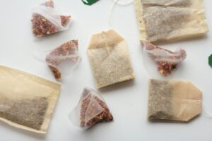 This image features an assortment of tea bags scattered across a clean, white surface. It shows a mix of traditional rectangular paper pouches and modern mesh pyramid bags filled with colorful herbal blends.