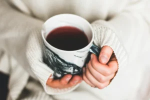 A person wearing a cozy, white knit sweater holds a marble-patterned mug filled with a dark red beverage. The close-up shot focuses on their hands gripping the cup, evoking a warm and comforting atmosphere.