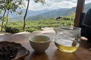 Glass pitcher and cup of tea on a wooden table overlooking a tea plantation.