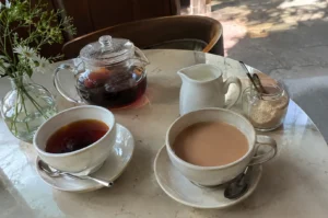 Tea service on a marble table with a glass teapot, cups of black and milk tea, and milk pitcher.