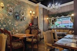 Vintage restaurant dining room with floral wallpaper, crystal chandelier, and damask armchairs.