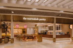 Illuminated modern storefront of The Marmalade Pantry with wood paneling and warm ambient lighting.