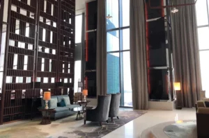 Double-height luxury lounge with tall windows, beige curtains, and dark wood lattice paneling.