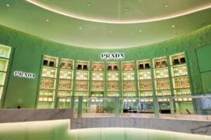 Elegant Prada Cafe interior in pastel mint green featuring curved display cabinets filled with packaged delicacies behind a white marble service counter.