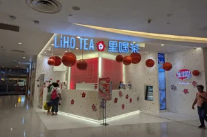 Storefront of a LiHO TEA outlet inside a shopping mall, featuring bright illuminated signage, suspended red spherical decorations, and a white service counter decorated with floral accents.