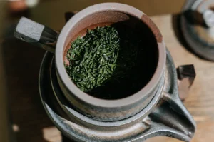 Close-up top-down view of dark green loose leaf green tea inside a traditional ceramic teapot filter basket.
