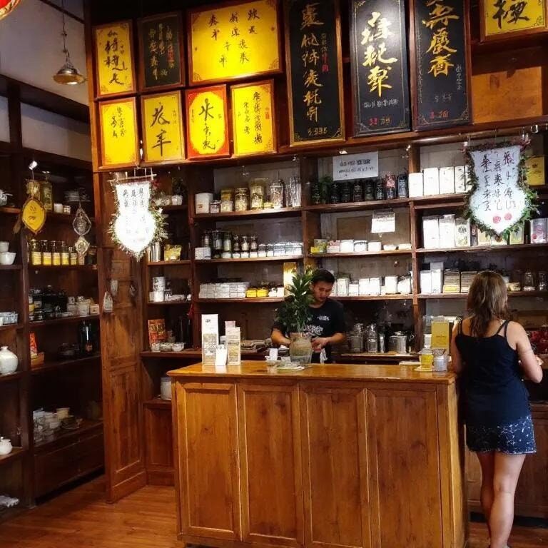 The image depicts a traditional tea shop interior in Singapore's Chinatown, featuring wooden shelves filled with a variety of loose leaf teas, inviting tea lovers to explore the natural goodness and refreshing flavours of green teas and oolong. The tranquil atmosphere offers a perfect moment for indulging in a cup of crafted tea, making it a delightful place to immerse oneself in the world of tea.