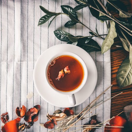 A cup of herbal tea with a cluster of dried lavender flowers sits on a wooden table.