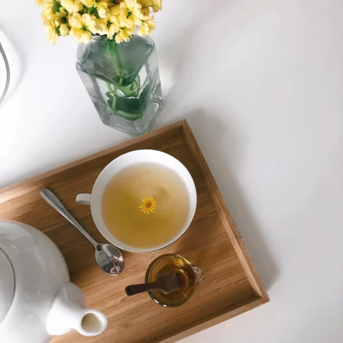 A delicate cup of tea with a blooming flower adorns a vintage wooden tray.